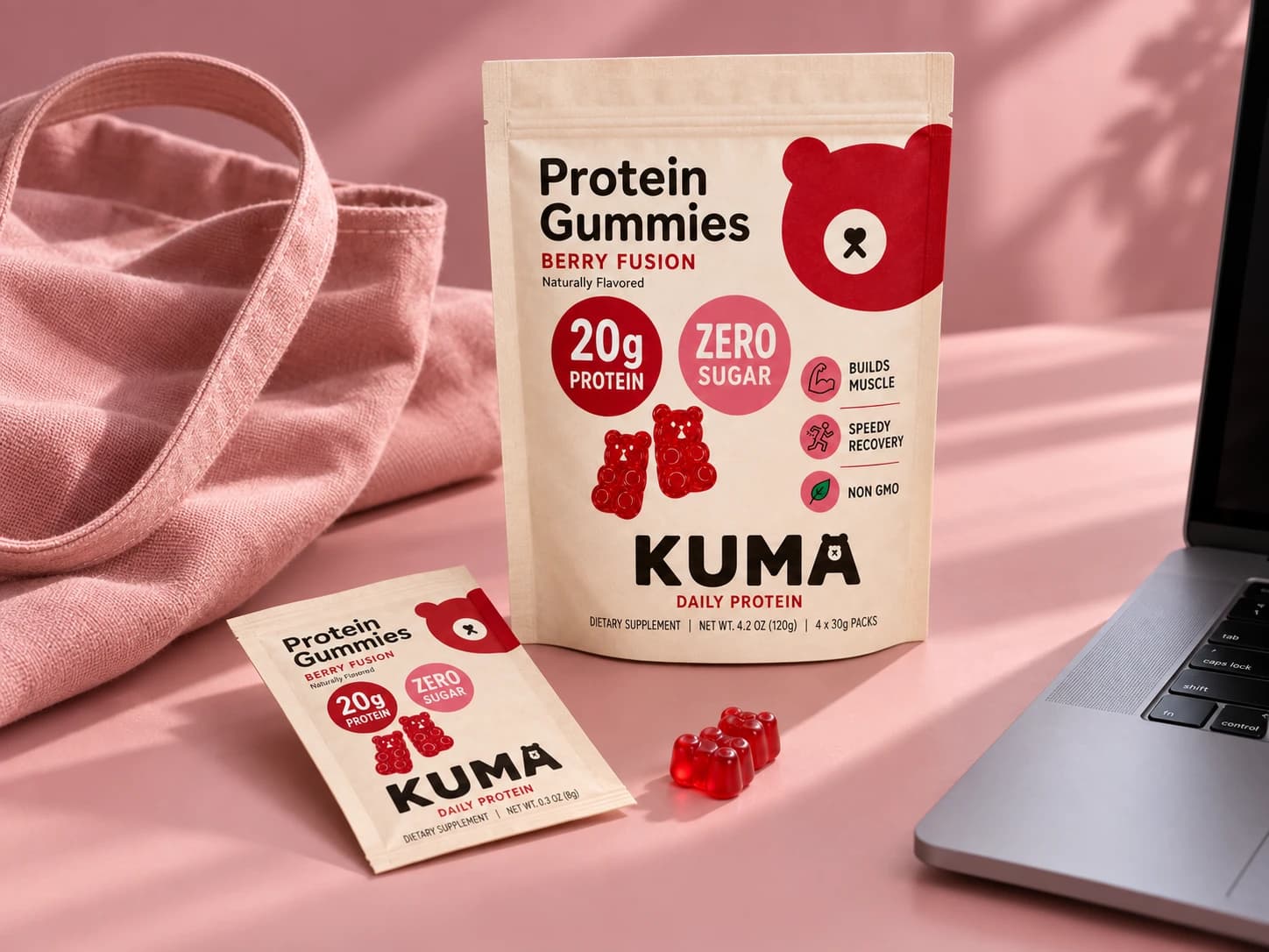 Kuma pouch, sachet, and red gummies on a blush pink desk beside a laptop